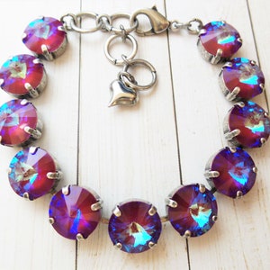 May include: A silver bracelet with a heart charm and a row of iridescent purple and blue round crystals.