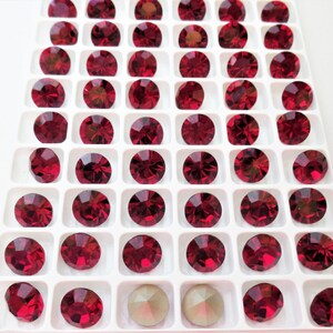 May include: A white tray with 60 small, round, red rhinestones arranged in a grid pattern. Two larger, round, iridescent rhinestones are in the bottom row.