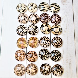 May include: Twenty-four round glass cabochons with various animal print designs, including leopard, zebra, tiger, and giraffe patterns. The cabochons are arranged in four rows of six, with each row featuring a different print.