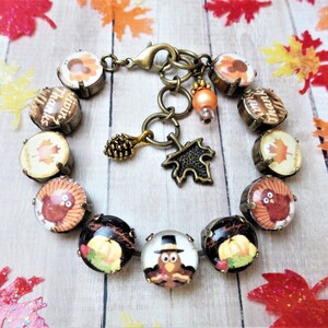 May include: A Thanksgiving themed bracelet with brown, gold, and orange glass beads featuring images of turkeys, pumpkins, and maple leaves. The bracelet has a lobster clasp and a charm with a pine cone and a leaf.