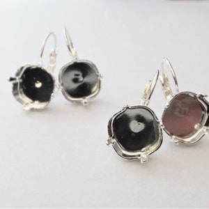 May include: A pair of silver earring settings with a round, open-back design. The settings are designed to hold a round stone or cabochon.
