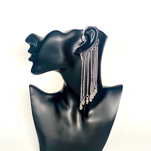 May include: Silver ear cuff with a dangling chain of small silver beads. The ear cuff is designed to wrap around the upper ear and has a small skull charm at the top.