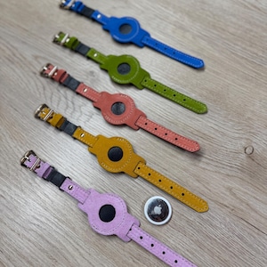 Può includere: Cinque cinturini in pelle in stile orologio per dispositivi di tracciamento in blu, verde, corallo, giallo e lavanda, ciascuno con un ritaglio circolare centrale, una fibbia in metallo argentato e un dispositivo di tracciamento argentato con logo Apple.