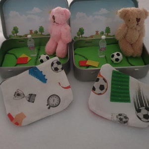 Tiny 8cm teddy in pocket tin laying on green felt football pitch with football 100 percent cotton blanket teddy has a football yellow and red warning cards and a football. Personalisation is optional