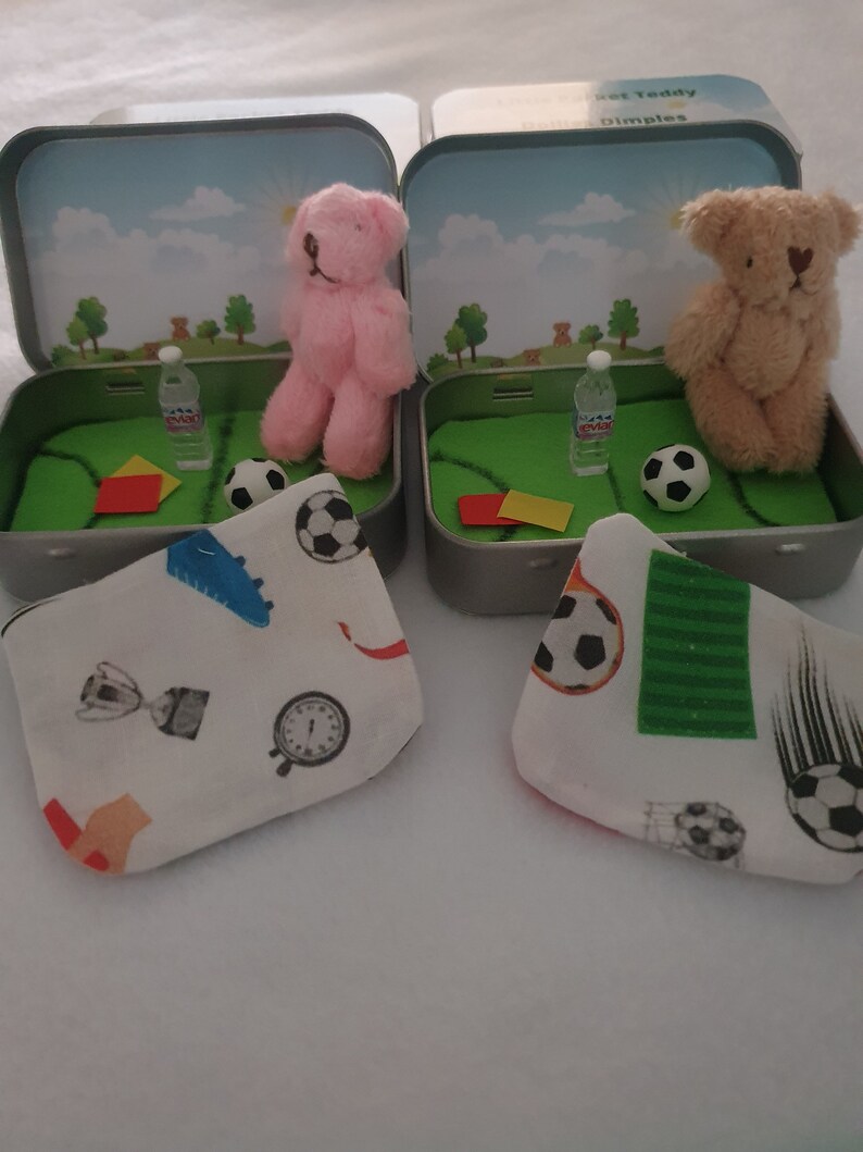 Tiny 8cm teddy in pocket tin laying on green felt football pitch with football 100 percent cotton blanket teddy has a football yellow and red warning cards and a football. Personalisation is optional