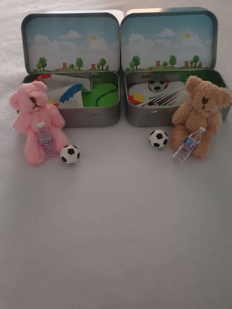 Tiny 8cm teddy in pocket tin laying on green felt football pitch with football 100 percent cotton blanket teddy has a football yellow and red warning cards and a football. Personalisation is optional