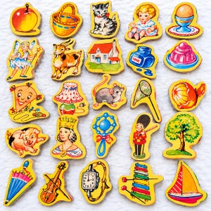 May include: A collection of twenty-five wooden cutout shapes featuring colourful illustrations of an apple, basket, kitten, child, egg, fairy, goat, house, ink bottle, jelly, kite, lamp, mouse, net, orange, pig, queen, rattle, soldier, tree, umbrella, violin, watch, xylophone, and sailboat.