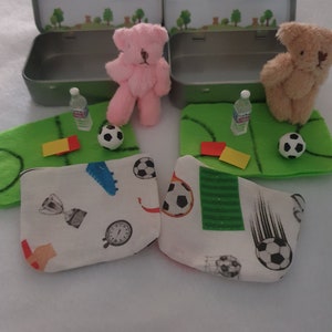 Tiny 8cm teddy in pocket tin laying on green felt football pitch with football 100 percent cotton blanket teddy has a football yellow and red warning cards and a football. Personalisation is optional
