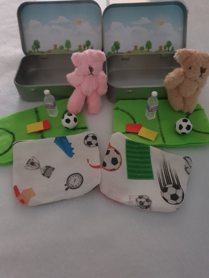 Tiny 8cm teddy in pocket tin laying on green felt football pitch with football 100 percent cotton blanket teddy has a football yellow and red warning cards and a football. Personalisation is optional