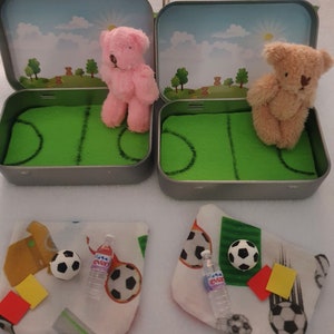 Tiny 8cm teddy in pocket tin laying on green felt football pitch with football 100 percent cotton blanket teddy has a football yellow and red warning cards and a football. Personalisation is optional
