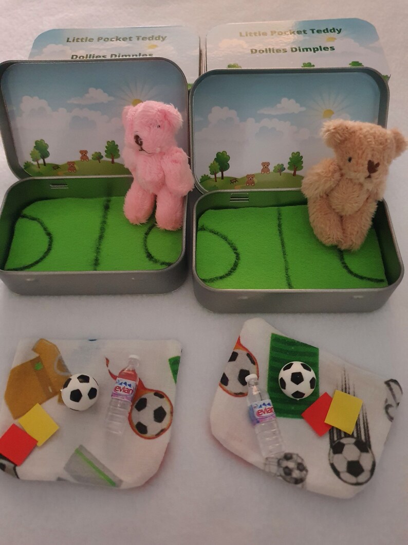 Tiny 8cm teddy in pocket tin laying on green felt football pitch with football 100 percent cotton blanket teddy has a football yellow and red warning cards and a football. Personalisation is optional