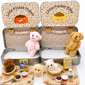 Peut inclure: Deux boîtes en métal étiquetées Little Pocket Puppy et Little Pocket Kitty. La boîte à chiot contient un ours en peluche rose et des perles formant le nom GRACIE. La boîte à chaton contient un ours en peluche beige et des perles formant le nom HAMISH. Elles incluent des accessoires miniatures comme des bols, des peluches et des boîtes de nourriture.