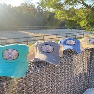 May include: Four different colored baseball caps with a donkey face patch on the front. The caps are sitting on a wicker chair.