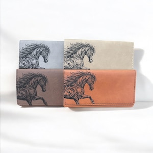 May include: Four different colored wallets with a black and white image of a horse running with a floral design. The wallets are in gray, beige, brown, and orange.