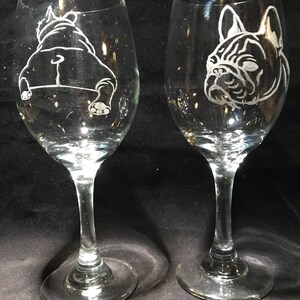 Op de afbeelding: Twee heldere glazen wijnglazen met gegraveerde afbeeldingen van Franse Bulldogs. Het ene glas heeft een bulldog die naar voren kijkt, terwijl het andere glas een bulldog heeft die van de kijker af kijkt.