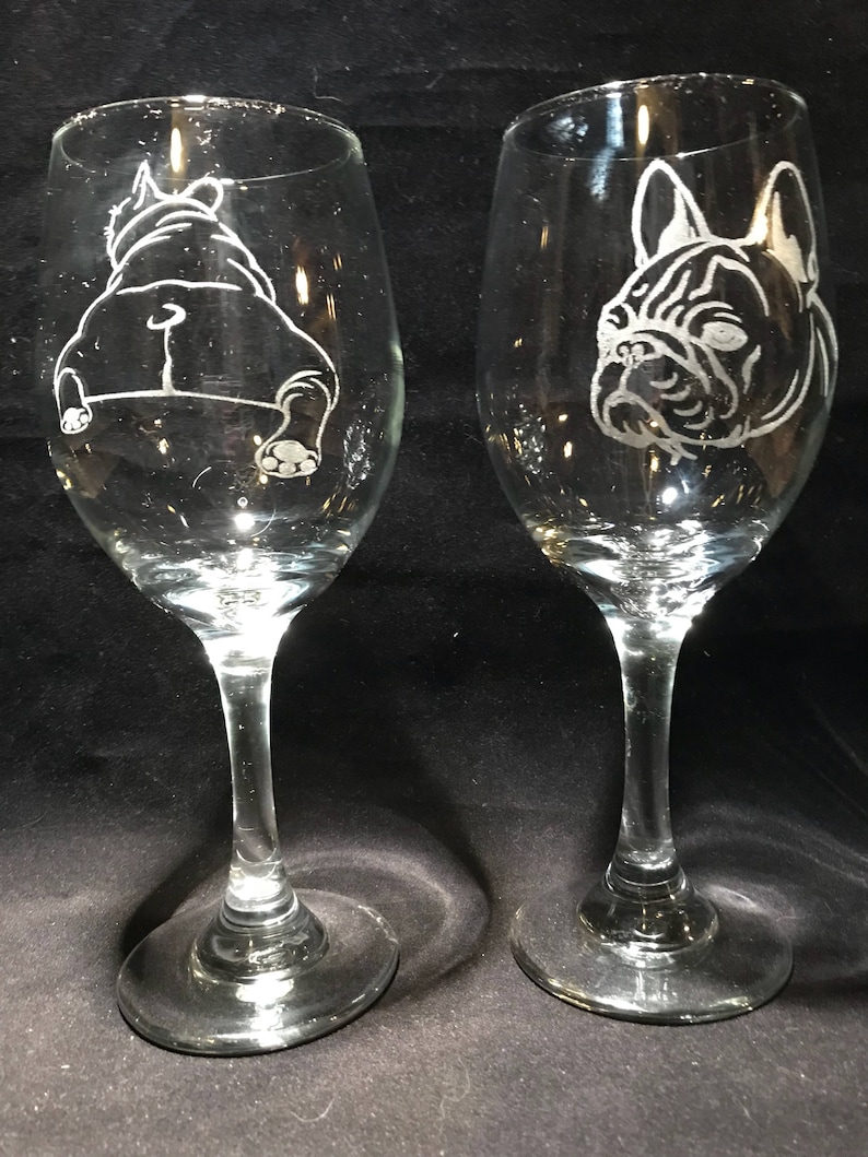Op de afbeelding: Twee heldere glazen wijnglazen met gegraveerde afbeeldingen van Franse Bulldogs. Het ene glas heeft een bulldog die naar voren kijkt, terwijl het andere glas een bulldog heeft die van de kijker af kijkt.