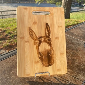 May include: A brown wooden cutting board with a laser-engraved image of a donkey's face. The donkey is looking directly at the camera with its mouth slightly open.