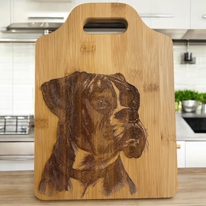 May include: A brown and black boxer dog is engraved on a natural bamboo cutting board with a handle. The cutting board is in a kitchen setting.