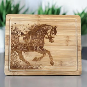 May include: A wooden cutting board with a laser-engraved design of a horse running through a field of flowers. The horse is wearing a saddle and bridle.
