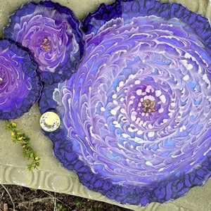 May include: A set of three purple and white resin coasters with a swirling, marbled design. The coasters have a dark purple border and a light purple center with white swirls.
