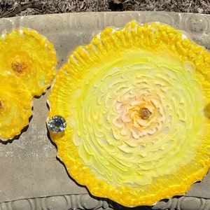 May include: A set of three yellow resin coasters with a swirl design and a matching larger tray. The coasters and tray have a glossy finish and are decorated with clear rhinestones.