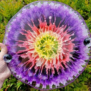 May include: A round, decorative tray with a floral design. The center is yellow and green, transitioning to red, pink, and purple. The tray has a glittery purple edge and two crystal handles.