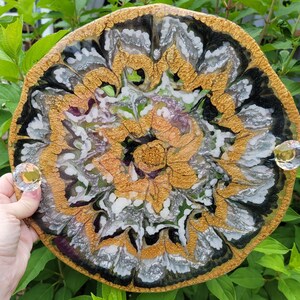 May include: A round resin tray with a black, white, and gold abstract floral design. The tray has a glossy finish and is perfect for serving snacks or displaying decorative items.