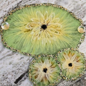 May include: A decorative resin serving tray and two matching coasters. The set features a light green background with a yellow floral design and a black center. The edges are adorned with gold and black glitter, and the tray has two clear, round embellishments.
