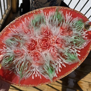 May include: Oval-shaped red resin tray with a floral design. The tray features a central arrangement of red roses and white and green accents. The rim is adorned with gold glitter, and it has two crystal handles.