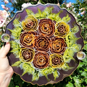 May include: A round resin tray with a dark purple background and a decorative design of yellow and orange flowers. The tray has a scalloped edge and two clear crystal knobs.