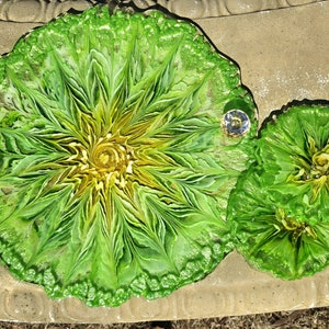 May include: Two green and yellow resin coasters with a swirling, abstract design. The coasters have a raised, textured edge.