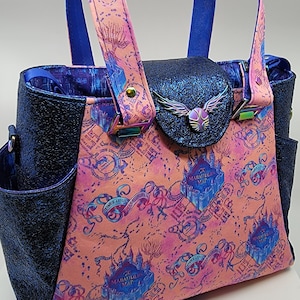 May include: A tote bag with a pink and blue map design, featuring a blue glitter flap with a winged emblem. The bag has blue handles and side pockets, with a matching pink and blue strap. The bag's design includes castle illustrations.