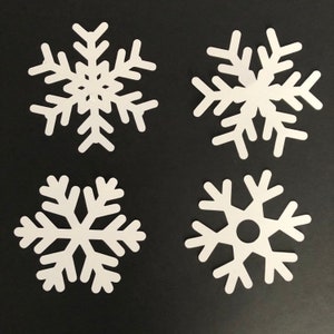 May include: Four white snowflake cutouts arranged in a grid. Each snowflake features a distinct geometric pattern with six symmetrical arms. The top left and top right snowflakes have intricate branching designs, while the bottom two have simpler shapes.