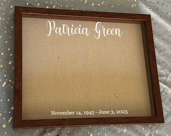 Peut inclure: Un cadre en bois rectangulaire avec un fond en tissu beige. Le nom "Patricia Green" est écrit en blanc en haut. Les dates "November 14, 1945 - June 3, 2025" sont imprimées en blanc en bas.