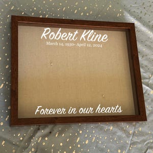 Puede incluir: Un marco conmemorativo con un marco de madera marrón. El fondo es de tela beige. El texto blanco dice "Robert Kline, 14 de marzo de 1930 - 12 de abril de 2024" y "Forever in our hearts".