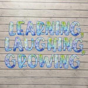 May include: A wooden background with the words "LEARNING, LAUGHING, GROWING" in large, colorful letters. The letters are blue with watercolor-style patterns in green and purple. The words are arranged in three lines.