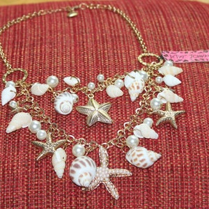 May include: Gold chain necklace with white seashells and starfish charms. The necklace has a "Juicy Couture" tag attached.