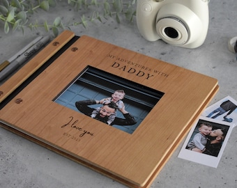 May include: A wooden photo album with a black spine and a photo frame on the front. The frame has a photo of a father and son. The album is engraved with the text "My Adventures with Daddy" and "I love you est. 2017".
