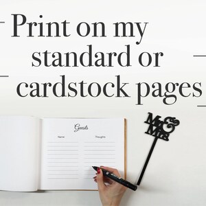 May include: A white guest book with the word "Guests" written in cursive on the cover. The book is open to a page with lines for names and thoughts. A black marker is being used to write in the book. A black "Mr. & Mrs." sign is in the background.