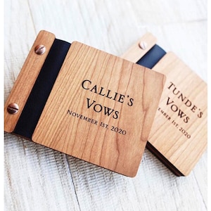 Puede incluir: Dos libros de votos de madera con cierres de cinta negra y tornillos plateados. El libro de la izquierda dice "Callie's Vows November 1st, 2020" y el libro de la derecha dice "Tunde's Vows December 1st, 2020".