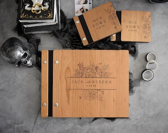 May include: A large wooden guestbook with a black spine and silver metal bolts, engraved with floral designs and the text JACK and REBEKA 9.26.98. Two smaller matching wooden vow books labelled HER VOWS and HIS VOWS are positioned above it.