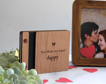 May include: A rectangular wooden photo album with a light brown wood grain finish. The front cover features a small laser-cut heart and the engraved text "You Make my heart happy". The album is bound with a dark spine and a metallic screw post fastener.