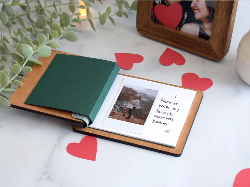 a small photo book with a handwritten note, a green paper, and a wooden frame, all placed on a marble surface.