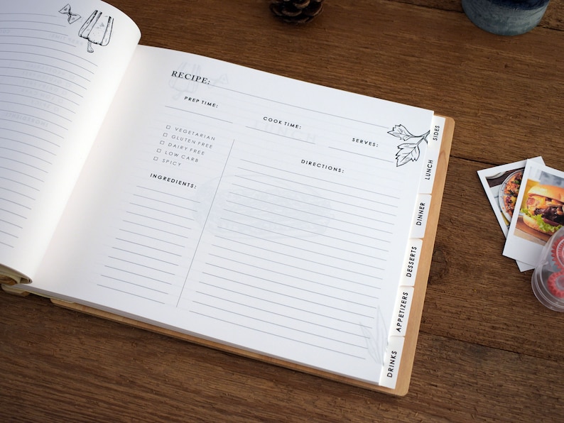May include: A white recipe book with a wooden spine and tabs for different meal categories, including drinks, appetizers, desserts, dinner, lunch, and sides. The book has lines for writing down recipes and includes checkboxes for dietary restrictions like vegetarian, gluten-free, dairy-free, low carb, and spicy.