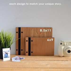 May include: Two wooden photo albums, one 8.5x11 inches and one 6x9 inches, with black ribbon closures and metal accents. The albums are on a wooden surface with a vintage camera and photos.