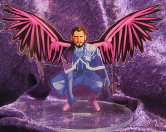 May include: A figurine of a person with dark hair and a beard wearing a blue and purple outfit with pink wings. The figurine is standing on a clear acrylic base.