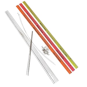 May include: Three yellow, orange, and pink wooden rulers with the text "Sweater Blockers" and "Woolstock" printed on them. The rulers are next to a pile of silver knitting needles and a small pile of silver tacks.