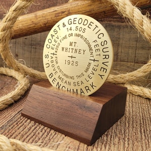 May include: A brass Coast & Geodetic Survey benchmark disk with the inscription "MT. WHITNEY 1925" and "14.505 FEET ABOVE MEAN SEA LEVEL 1373". The disk is mounted on a wooden base.
