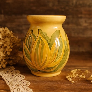 May include: A yellow ceramic vase with a floral design. The vase has a light yellow base with a detailed relief of yellow and green stylized flowers. A decorative item for the home.