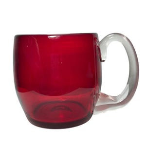 May include: A deep red glass mug with a rounded body and a clear, curved glass handle. The mug features a smooth, translucent finish that allows light to pass through the vibrant red material, highlighting the contrast with the clear handle.